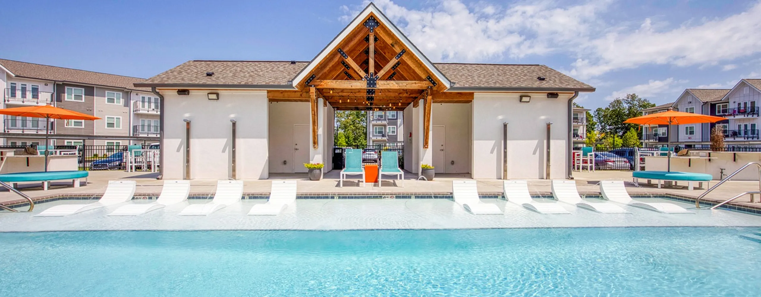 Luxurious apartment community with a sparkling swimming pool, modern lounging area, and vibrant outdoor amenities under a clear blue sky.