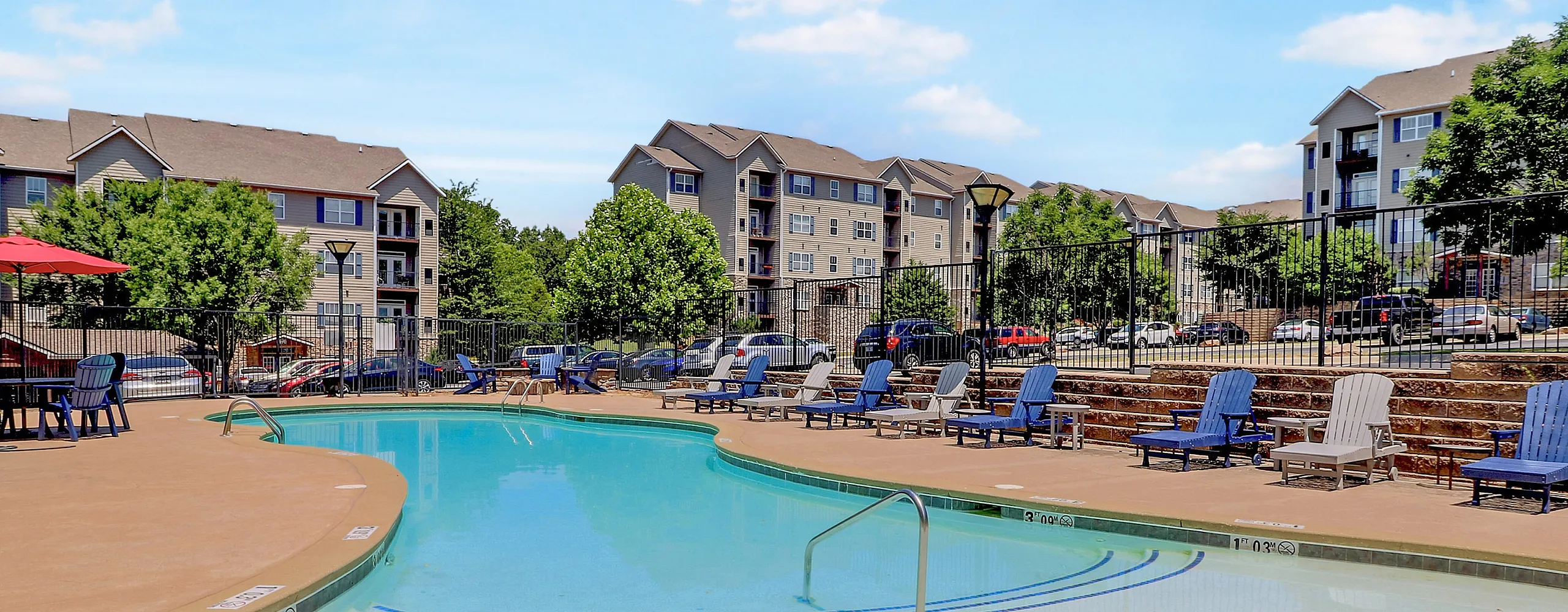 Inviting pool area surrounded by modern apartment buildings, featuring comfortable seating and vibrant parasols, perfect for relaxation and sunny afternoons.
