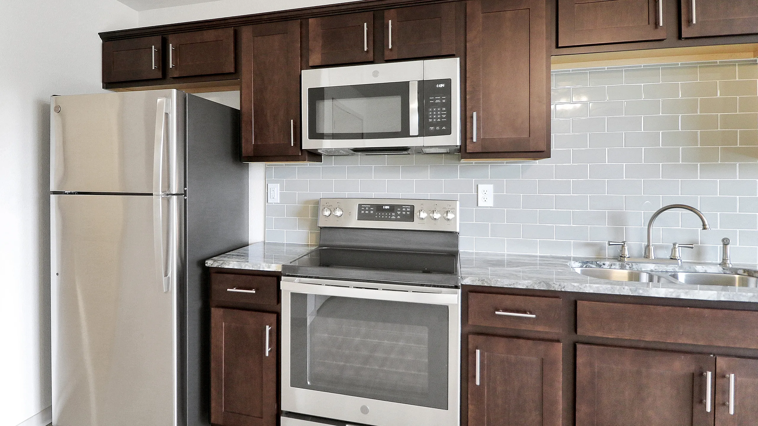 Modern kitchen with sleek stainless steel appliances, elegant dark wood cabinetry, and glossy subway tile backsplash.