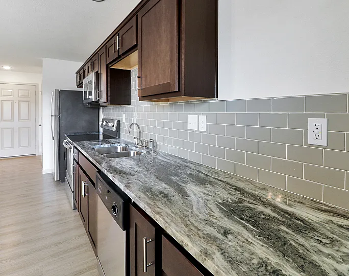 Modern kitchen with sleek granite countertops, stylish dark wood cabinets, and stainless steel appliances against a chic gray subway tile backsplash.