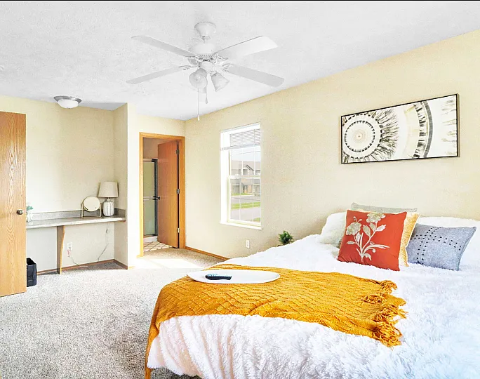 Inviting bedroom with cozy white bedding, colorful pillows, natural light through a window, and modern wall art.