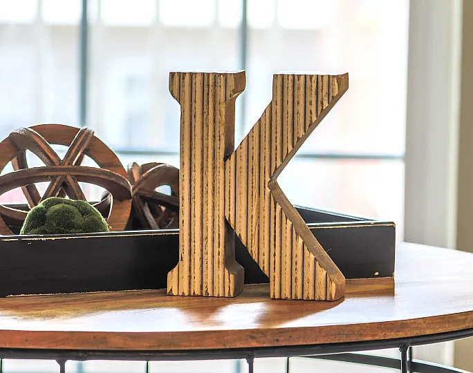 Chic interior decor featuring a stylish wooden letter 'K' next to artistic wooden and green moss accents on a sleek round table.