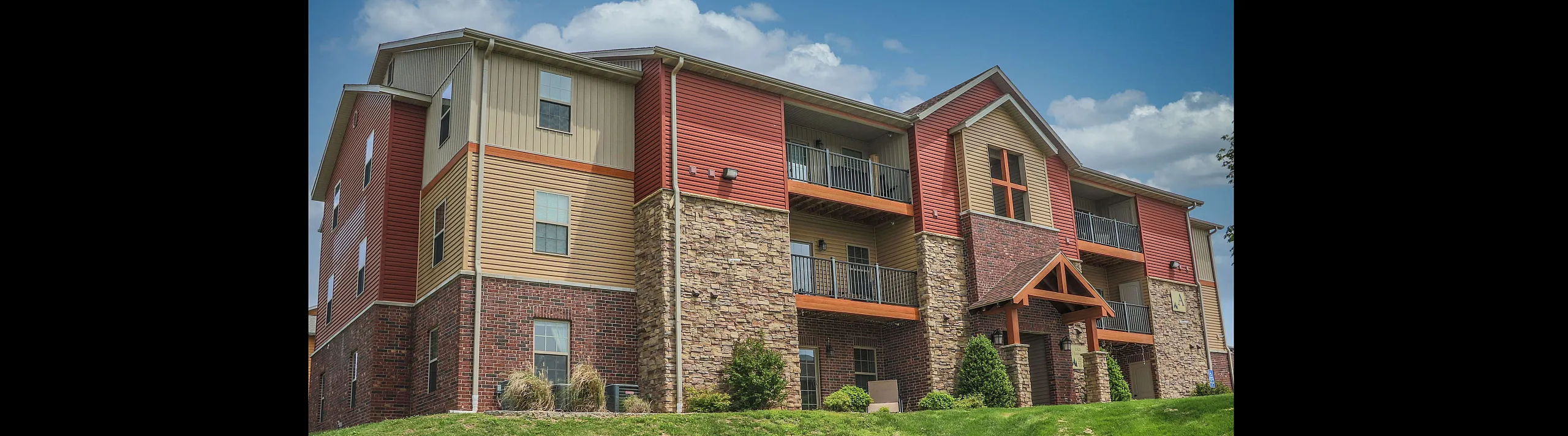 Charming apartment building showcasing a modern design with brick accents and a lush green lawn, perfect for comfortable living.
