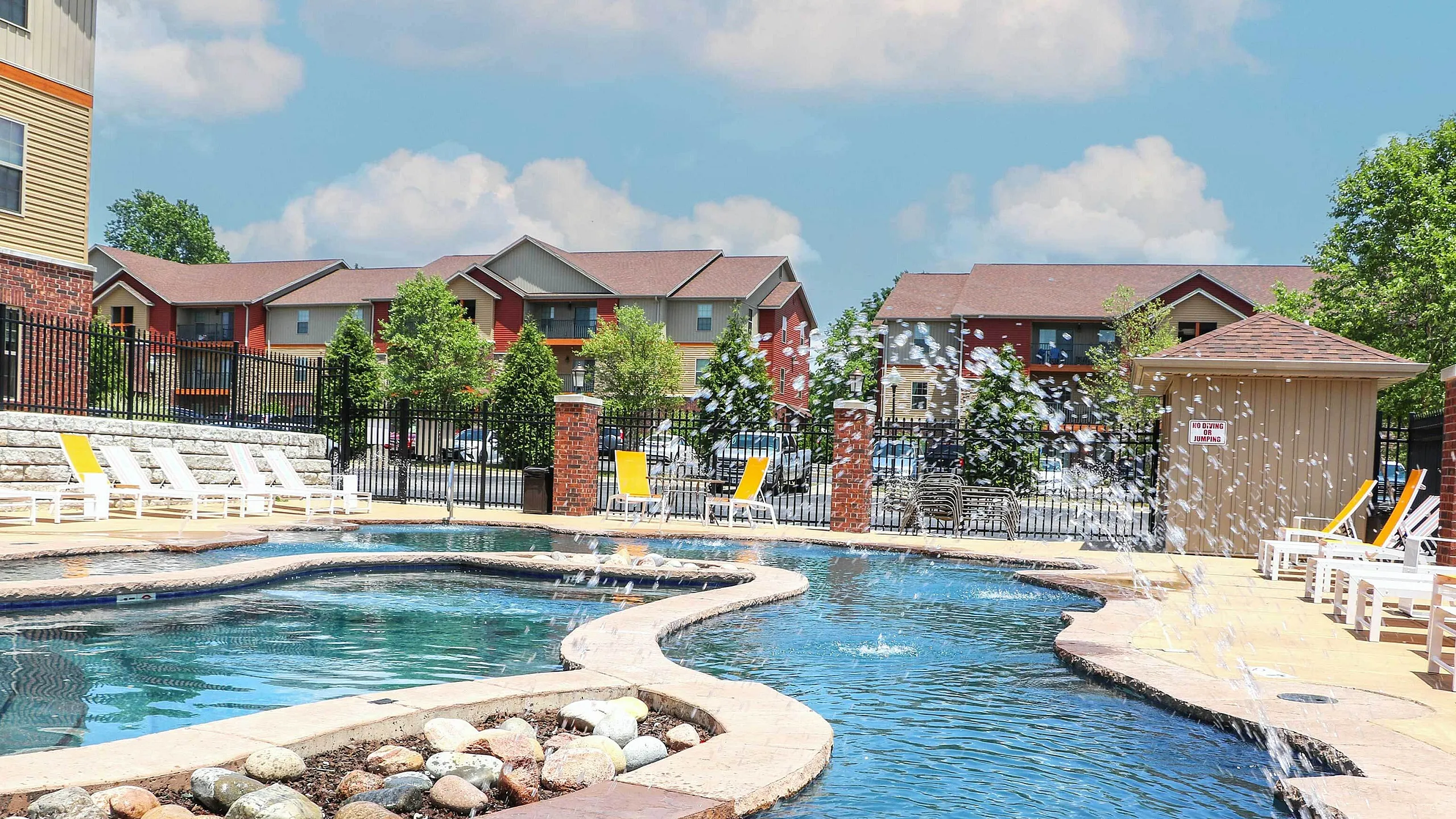 Luxurious apartment complex with a sparkling resort-style swimming pool, surrounded by comfortable lounge chairs and vibrant landscaping, perfect for relaxation and leisure.