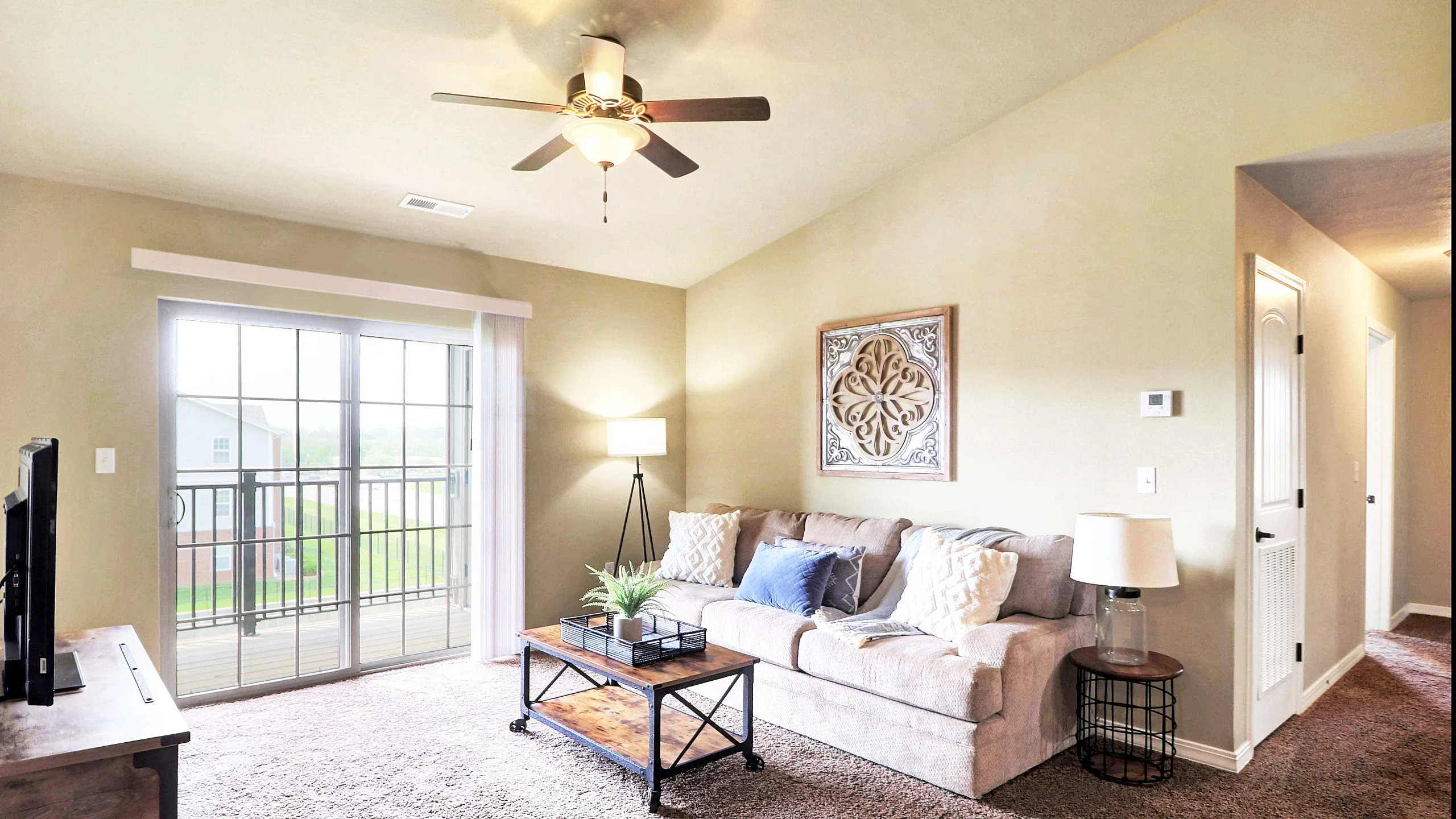 Inviting living room with stylish decor, plush carpet, and natural light streaming through sliding glass doors leading to a private balcony.