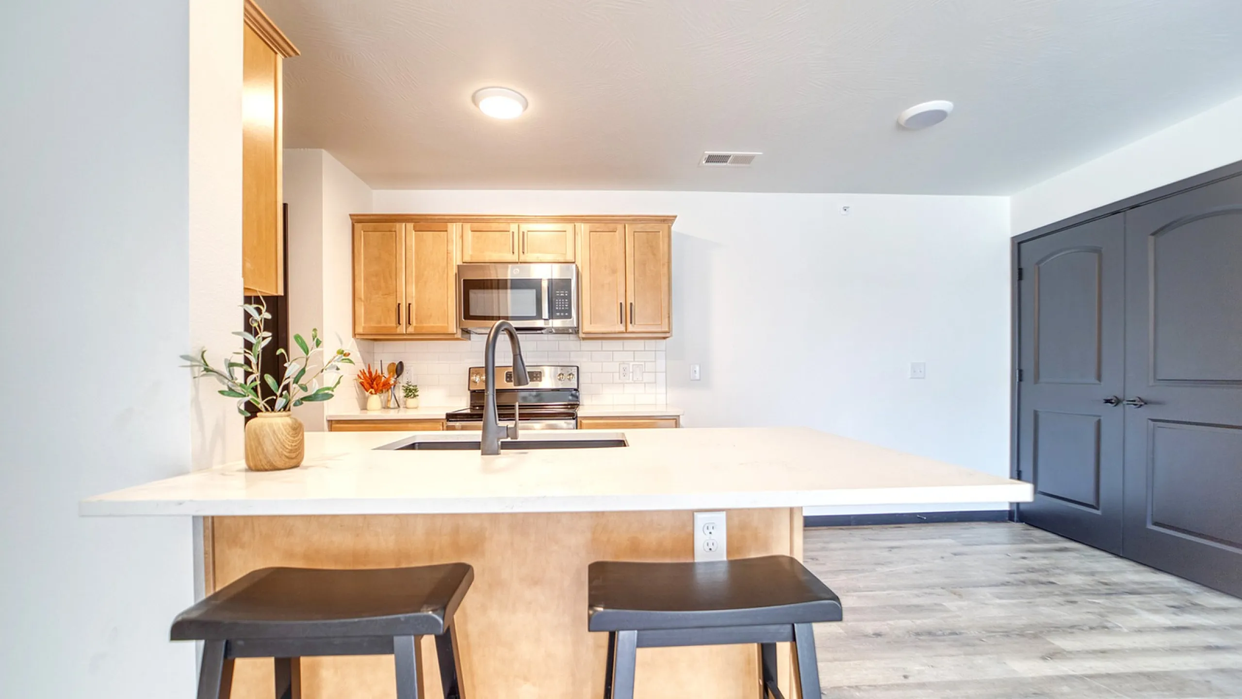 Modern kitchen with sleek countertops, elegant bar stools, and stylish cabinetry accented by a built-in microwave.