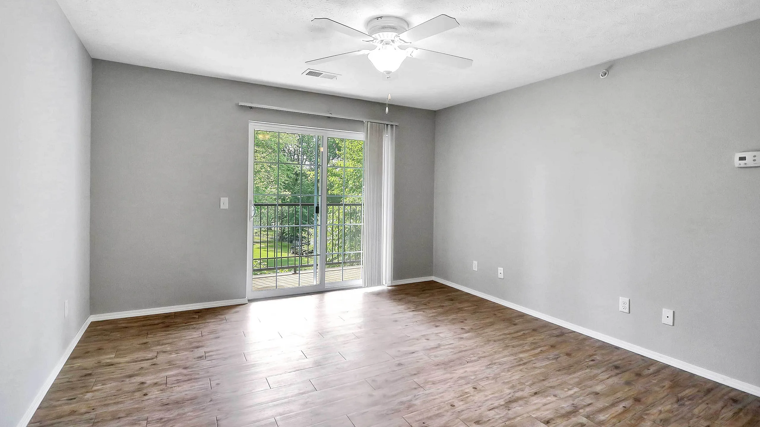 Bright, airy room with sleek wooden floors and a ceiling fan, opening to a scenic balcony through sliding glass doors.