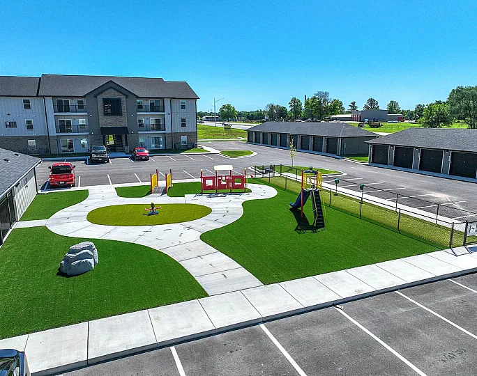 Inviting apartment complex with vibrant playground, lush green space, ample parking, and modern amenities.