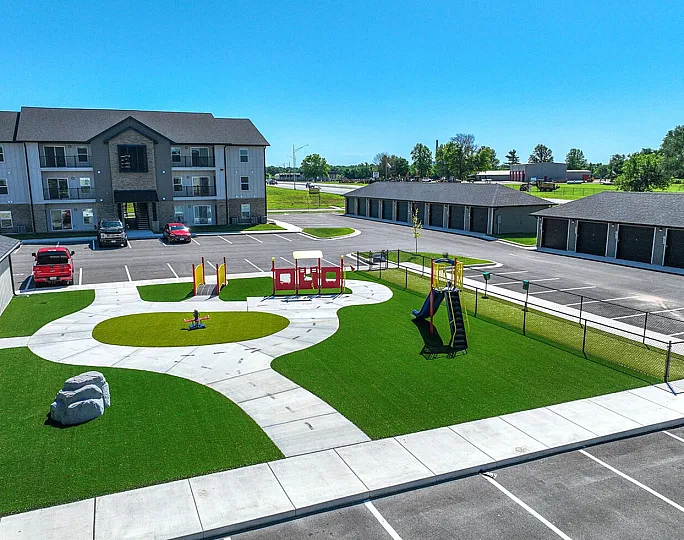 Inviting apartment complex with modern playground, lush green lawn, and convenient parking, perfect for families.