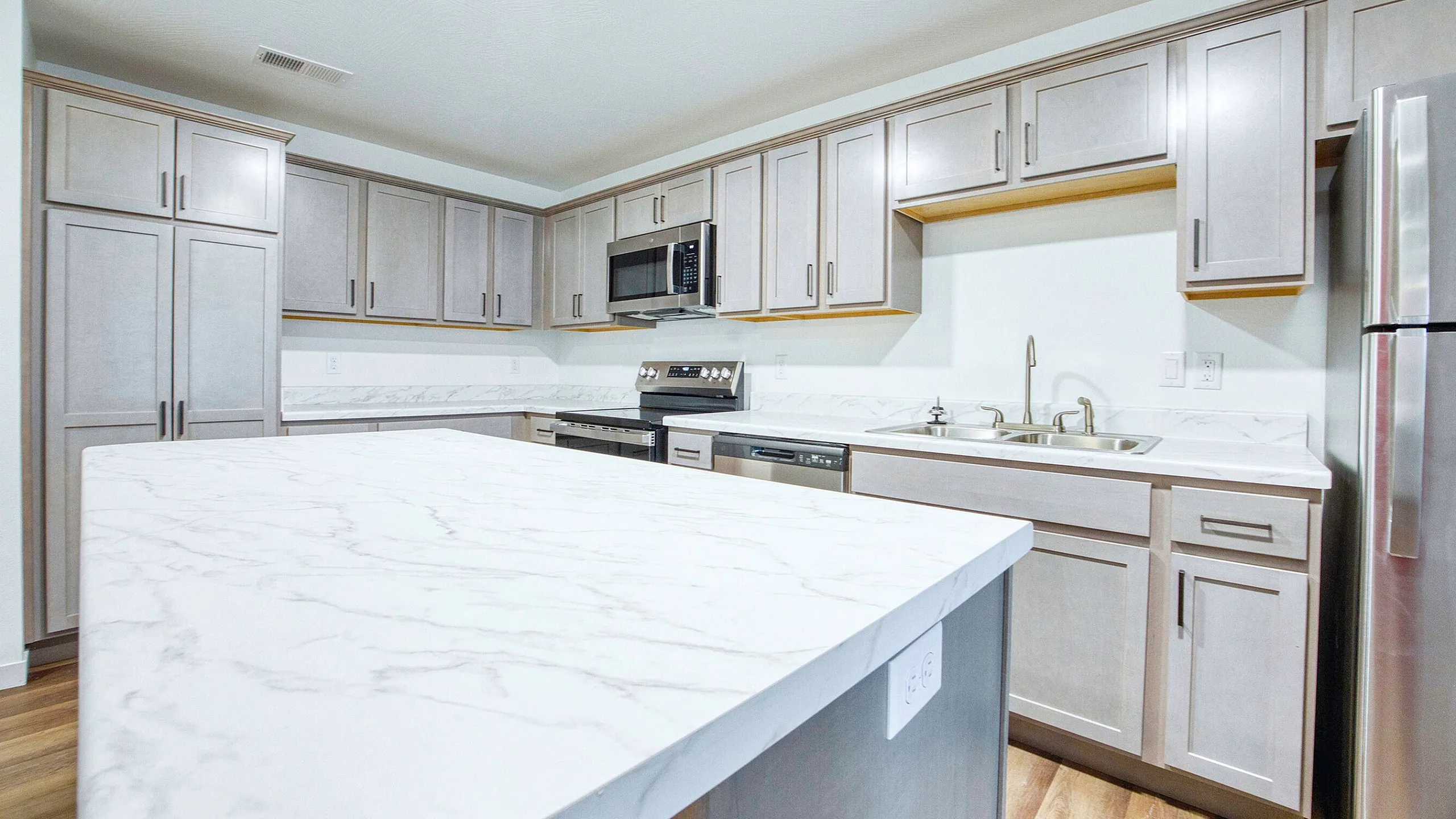 Modern kitchen with sleek white marble countertops, stainless steel appliances, and elegant cabinetry, offering a sophisticated cooking space.