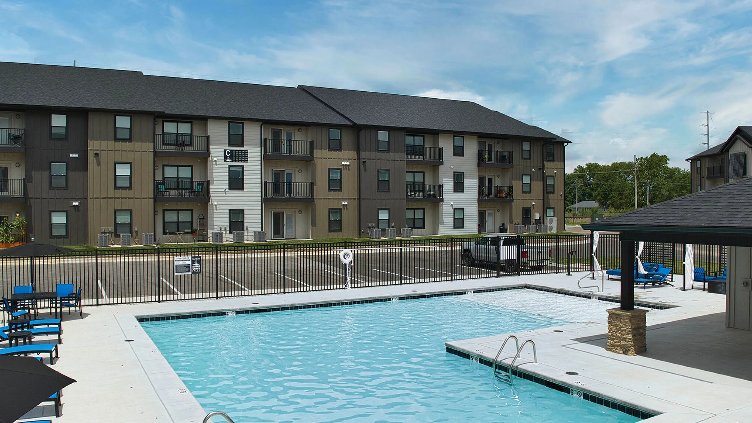 Luxurious apartment complex with a sparkling outdoor pool, stylish seating, and modern architecture under a bright blue sky.