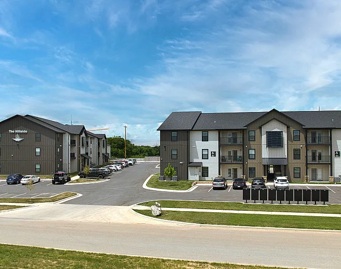 Modern apartment complex with spacious parking and attractive architecture under a bright blue sky.