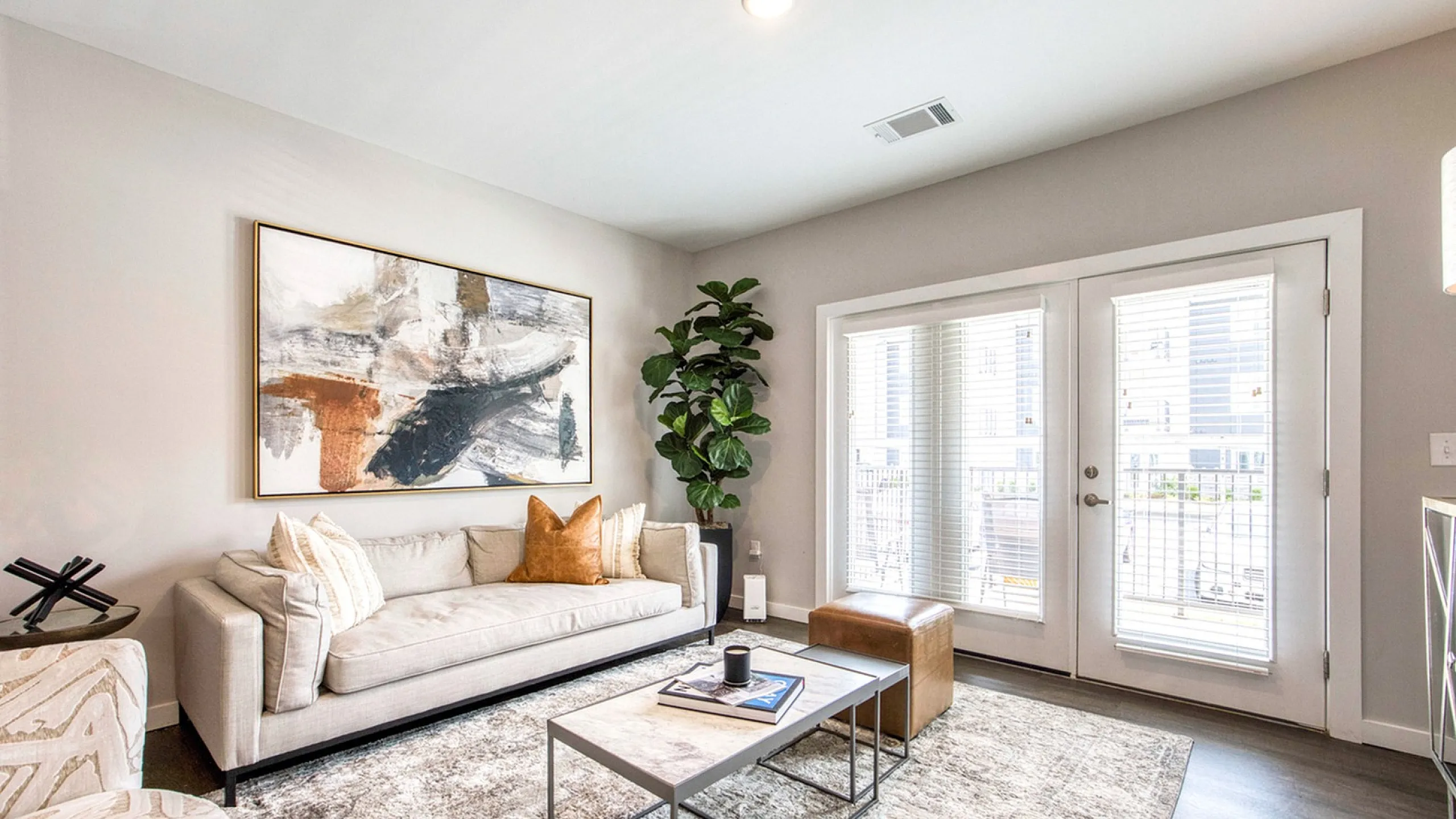 Bright and modern living room with stylish decor, large abstract art, and abundant natural light through French doors.
