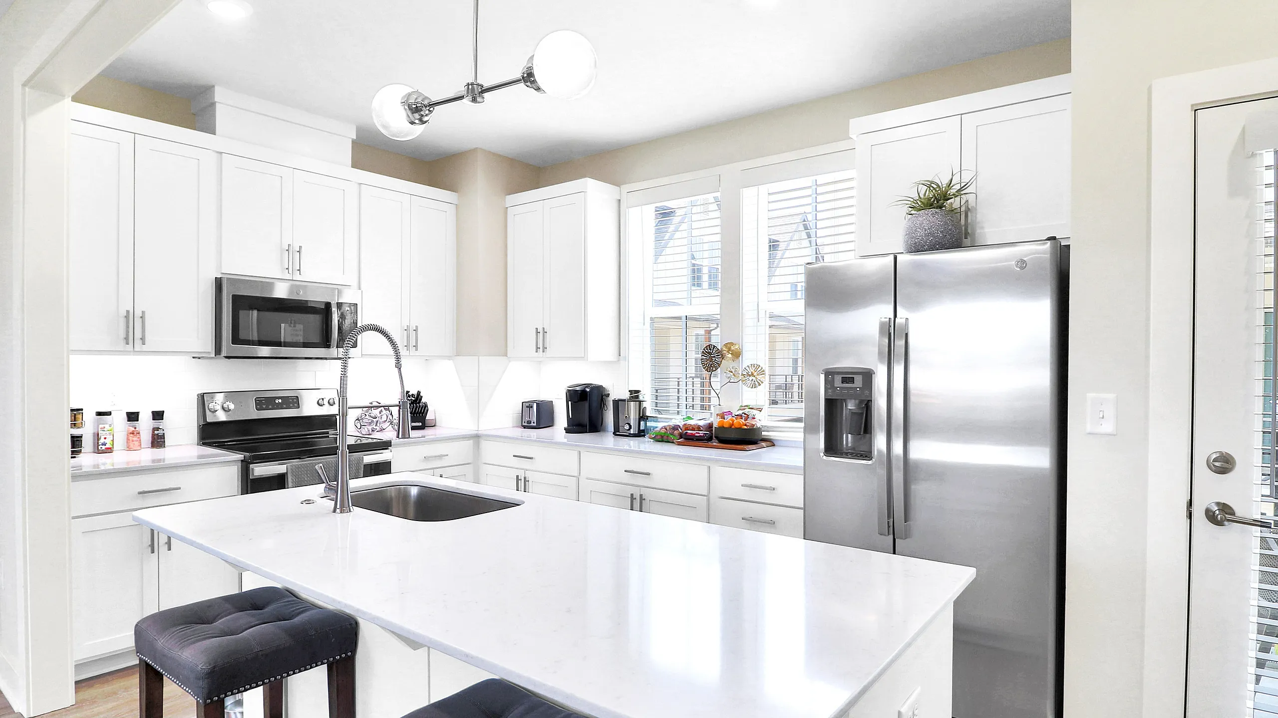 Bright and modern kitchen featuring sleek white cabinetry, stainless steel appliances, and a spacious island with stylish barstools.