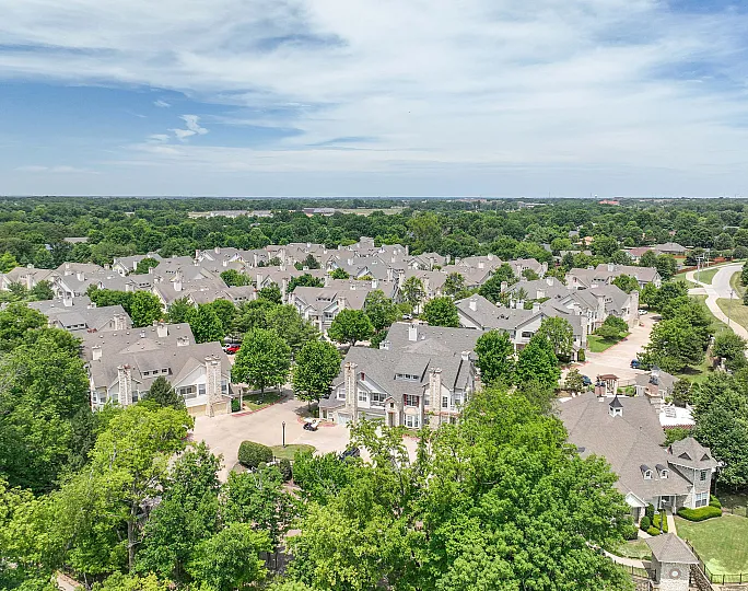 Charming aerial view of a beautifully nestled neighborhood surrounded by lush greenery, featuring elegant homes with landscaped yards under a stunning blue sky.