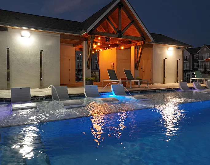 Elegant poolside at dusk with illuminated lounge chairs and a modern pavilion, perfect for relaxation and evening gatherings.