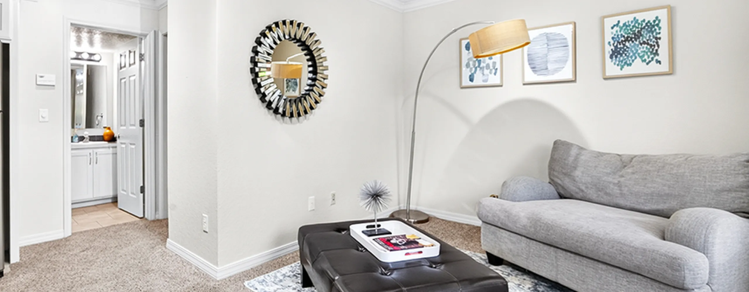 Inviting living room featuring plush gray sofa, stylish mirror, modern floor lamp, and sleek stainless steel refrigerator.