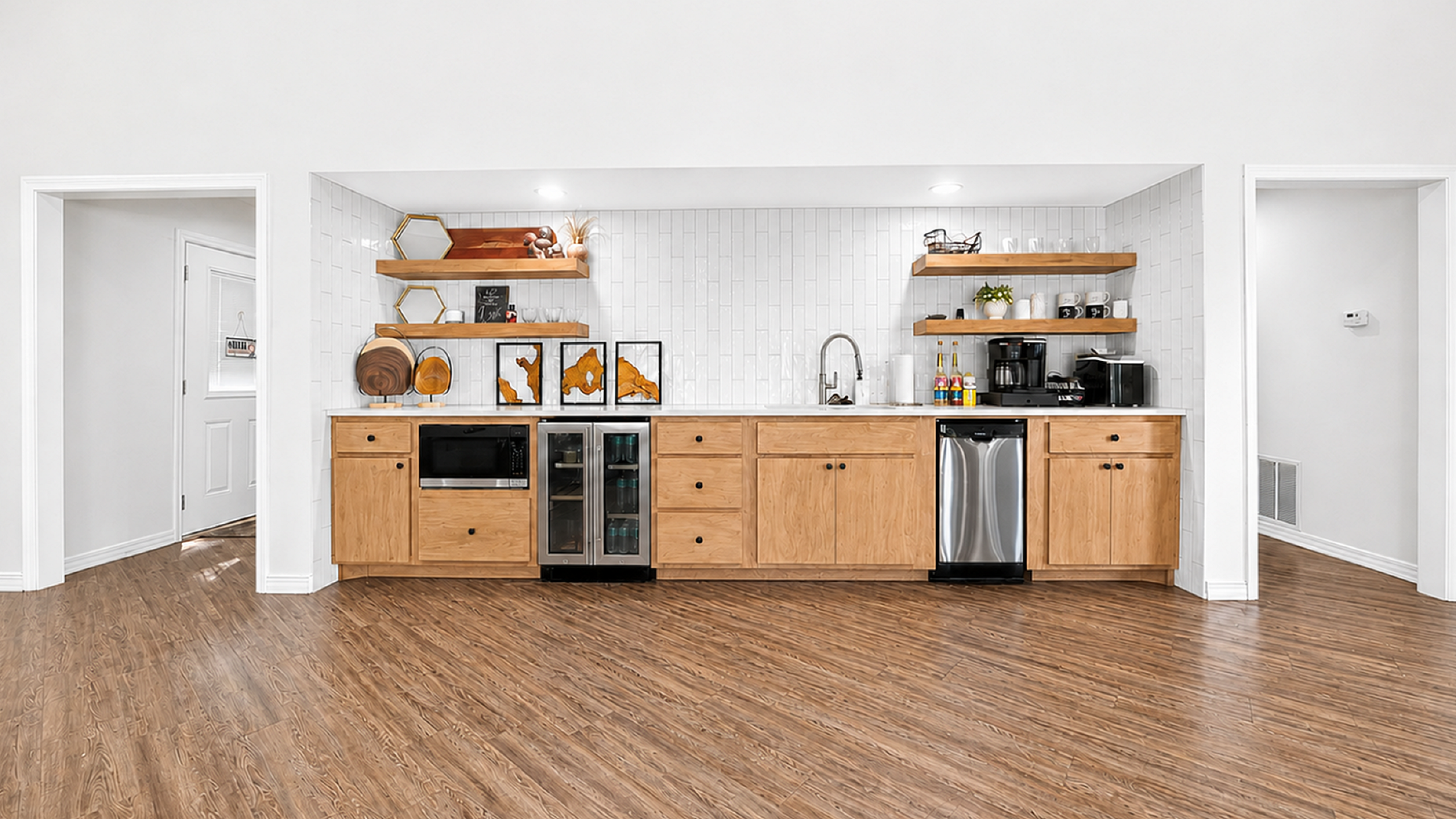 Sleek modern kitchen with light wood cabinetry, stainless steel appliances, and open shelving against a stylish tiled backsplash.