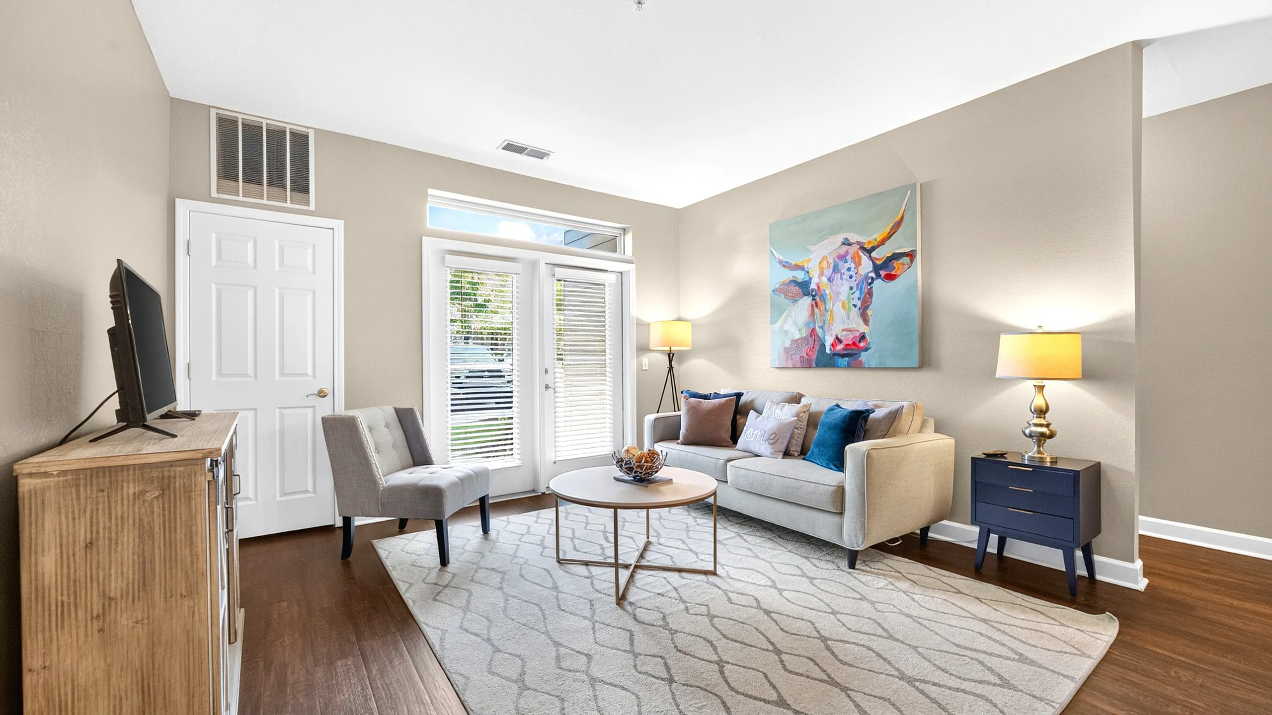 Bright and inviting living room featuring elegant hardwood floors, modern furnishings, and vibrant artwork, bathed in natural light through large patio doors.