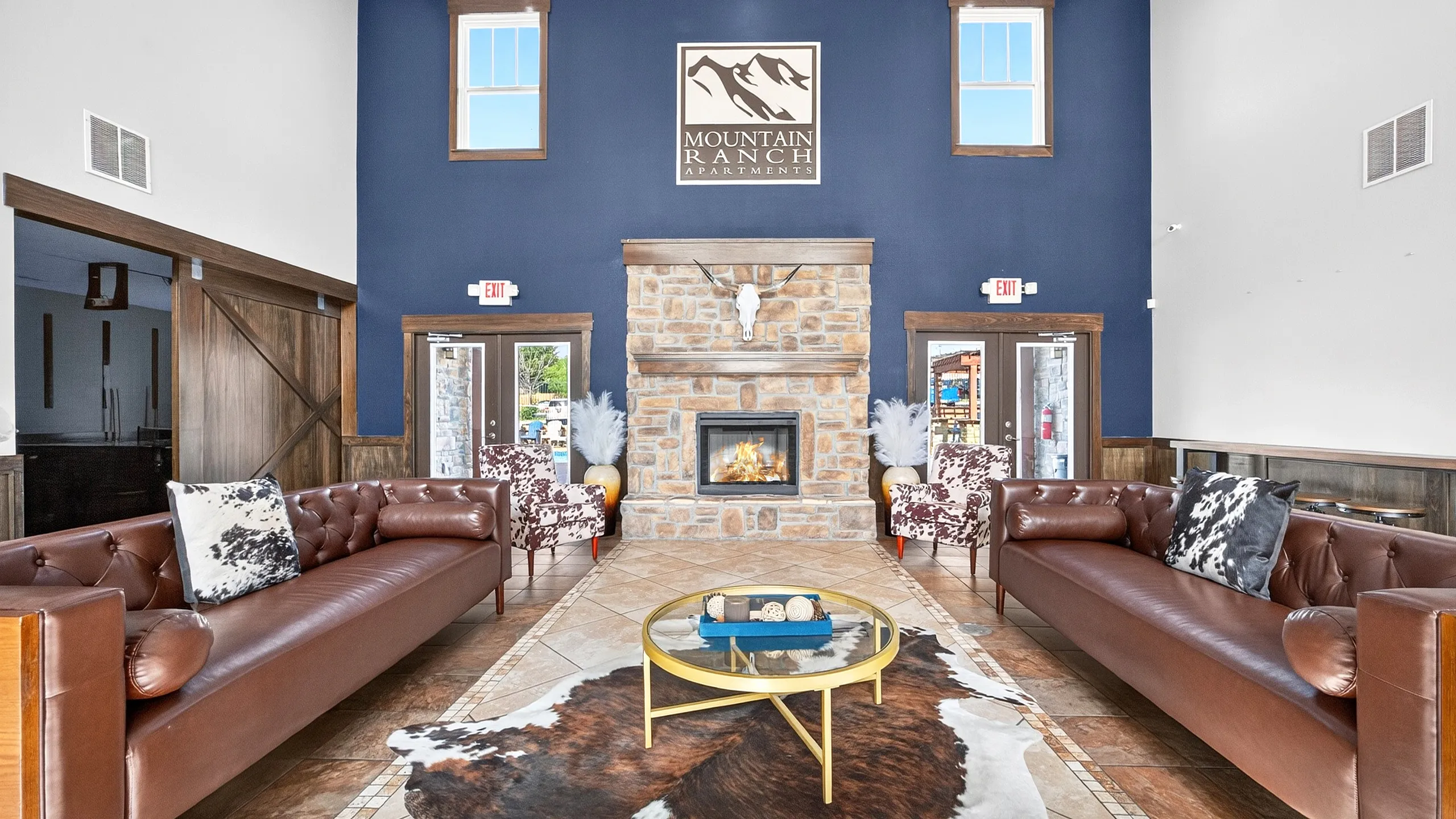 Inviting lounge area at Mountain Ranch Apartments featuring plush leather sofas, a cozy stone fireplace, and elegant decor with rustic charm.