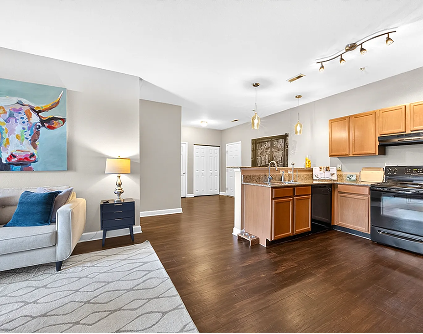 Bright open-concept living space with modern kitchen, hardwood floors, and vibrant wall art.