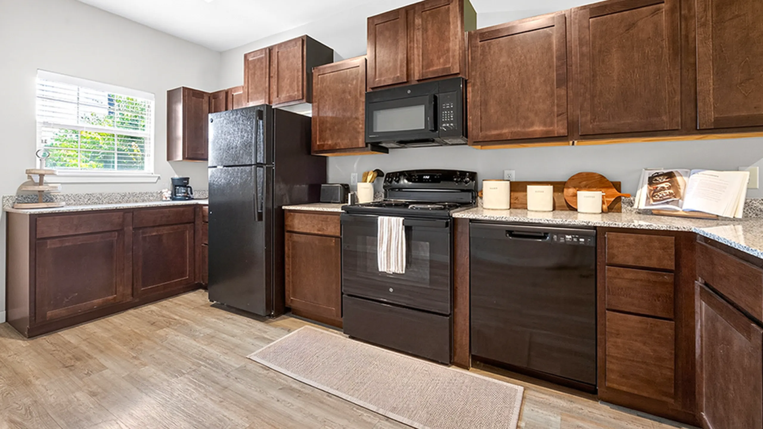 Modern kitchen with elegant dark wood cabinetry, granite countertops, and sleek black appliances, featuring ample natural light.