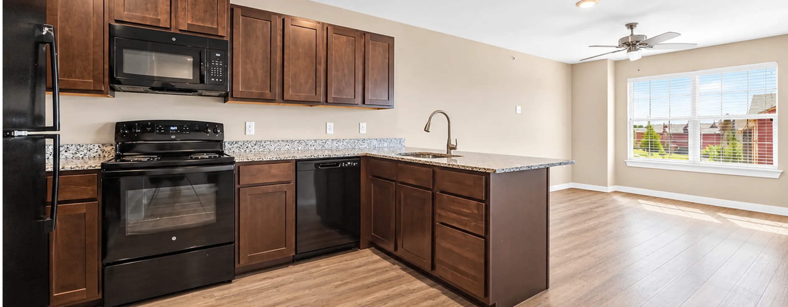 Bright, open-concept kitchen with rich wood cabinetry and sleek black appliances, adorned with granite countertops and large windows inviting natural light.