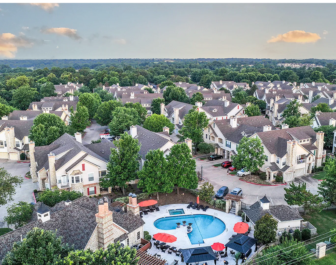 Charming suburban community with elegant townhomes nestled among lush trees, featuring a central swimming pool with cozy seating under vibrant umbrellas.
