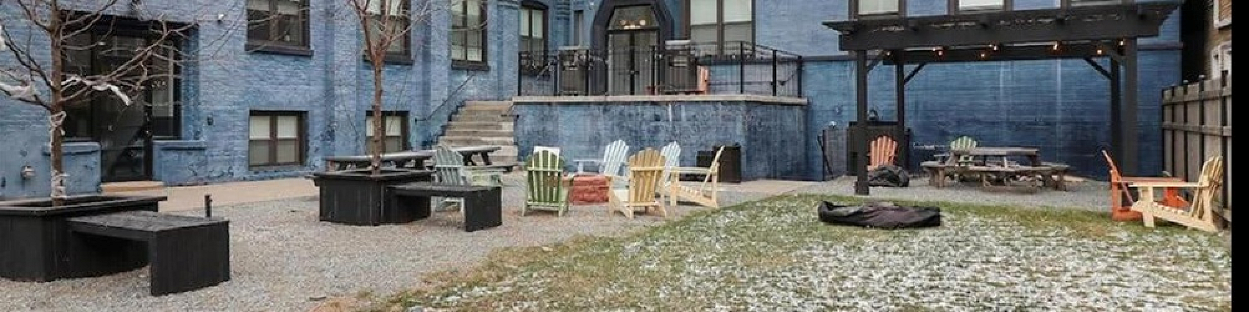 Charming apartment courtyard featuring a spacious open area with Adirondack chairs, tables, and vibrant blue exterior. Perfect for relaxing and social gatherings.