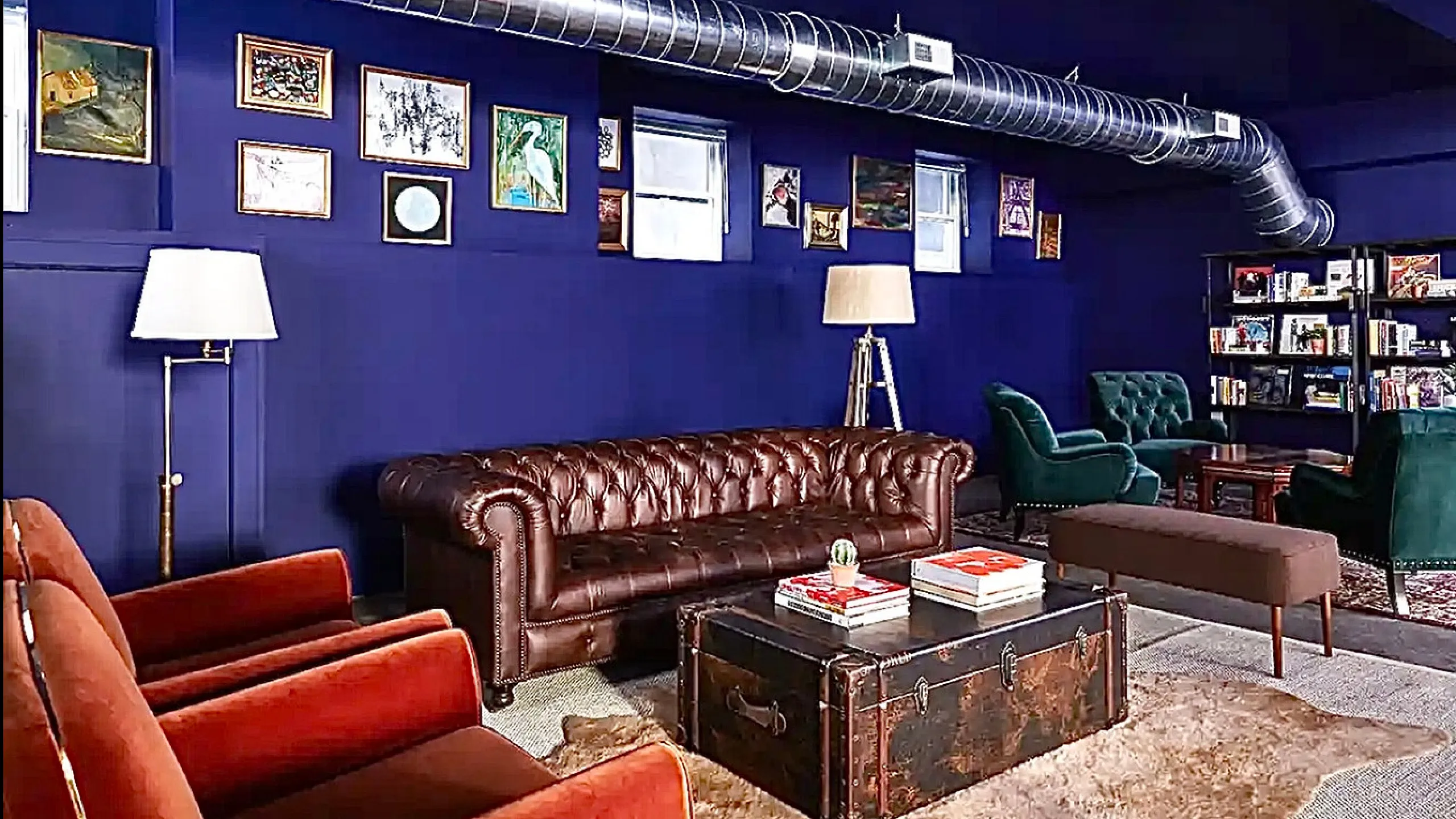 Chic living room with deep blue walls, featuring a classic leather sofa, vintage-style trunk coffee table, and eclectic artwork.