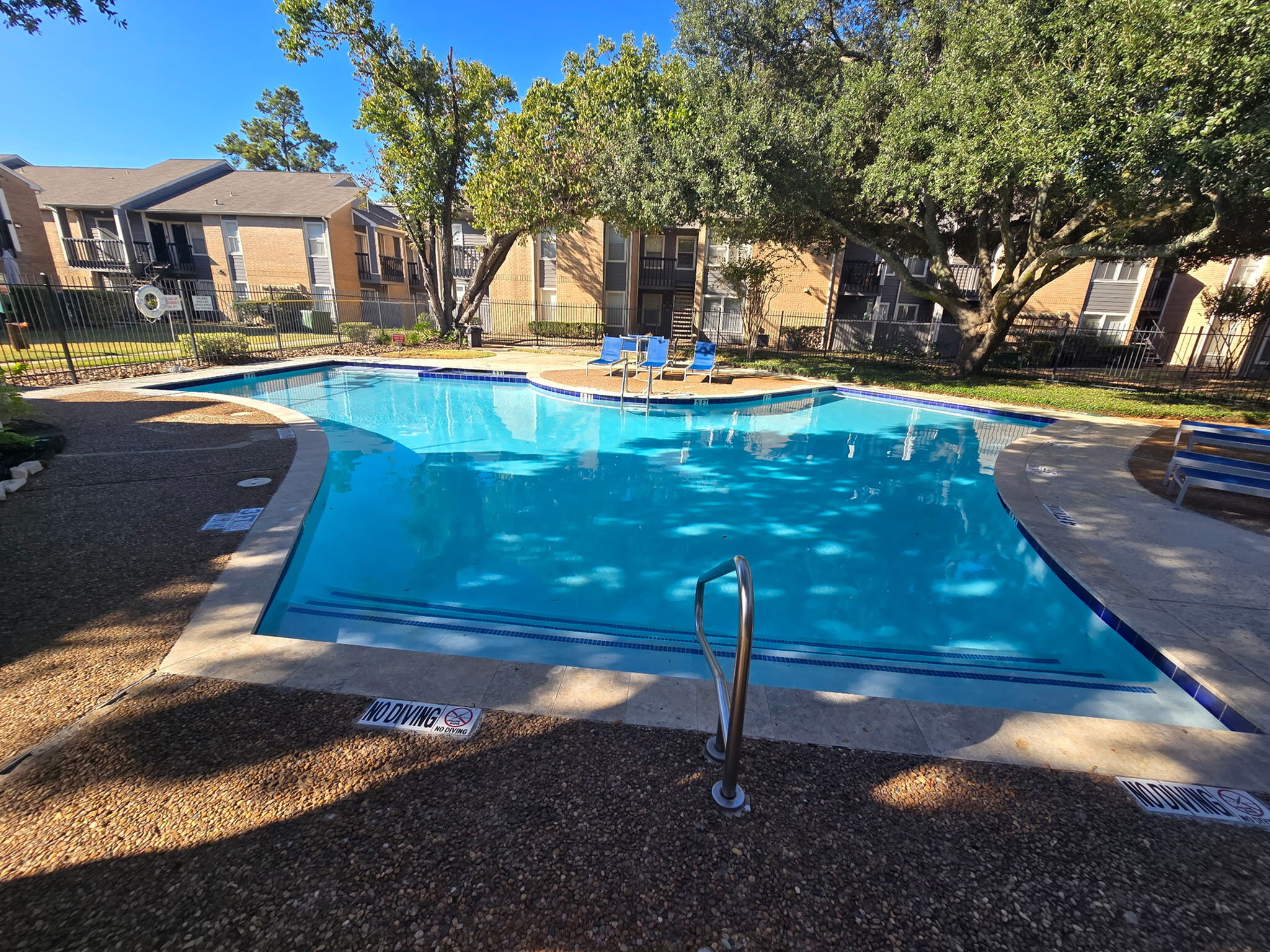 Inviting outdoor swimming pool surrounded by lush greenery and charming residential buildings, perfect for relaxation and leisure.