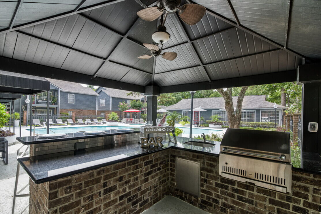 Charming outdoor bar and grill area overlooking a sparkling pool surrounded by elegant lounge chairs and lush greenery, perfect for entertaining and relaxation.