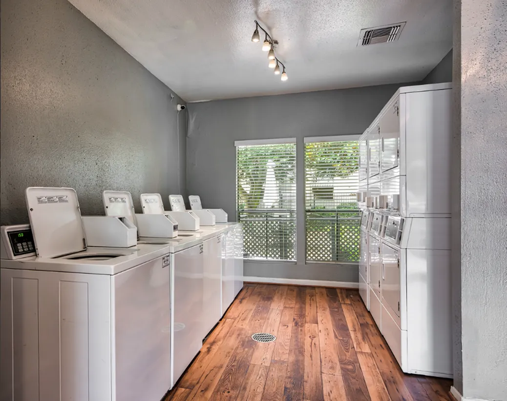 Modern laundry room with multiple sleek washing machines, wooden floors, and natural light from large windows.
