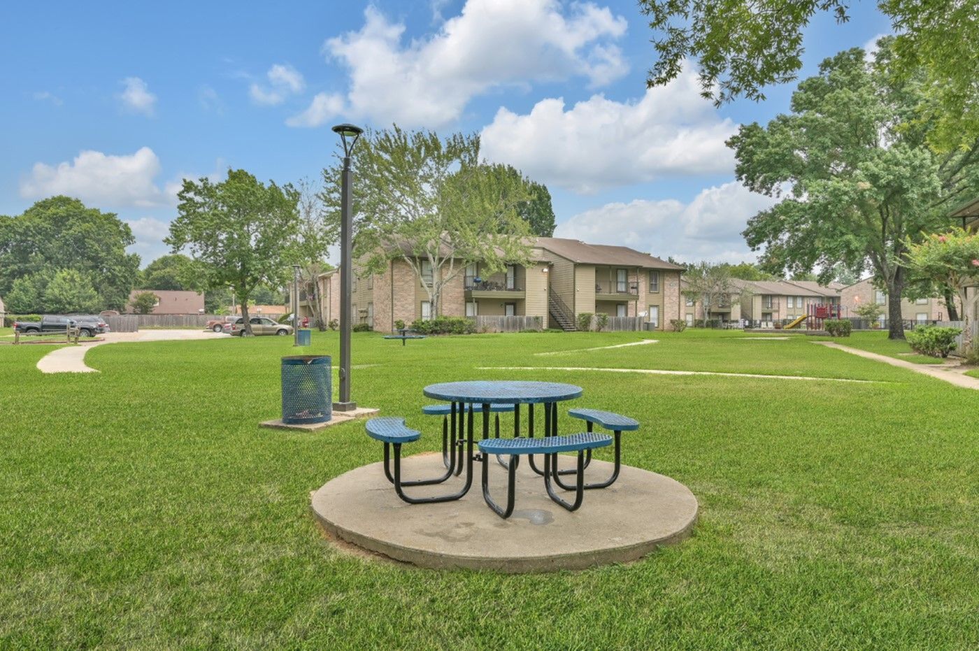 Charming apartment complex surrounded by lush greenery with a cozy picnic area under a clear blue sky.