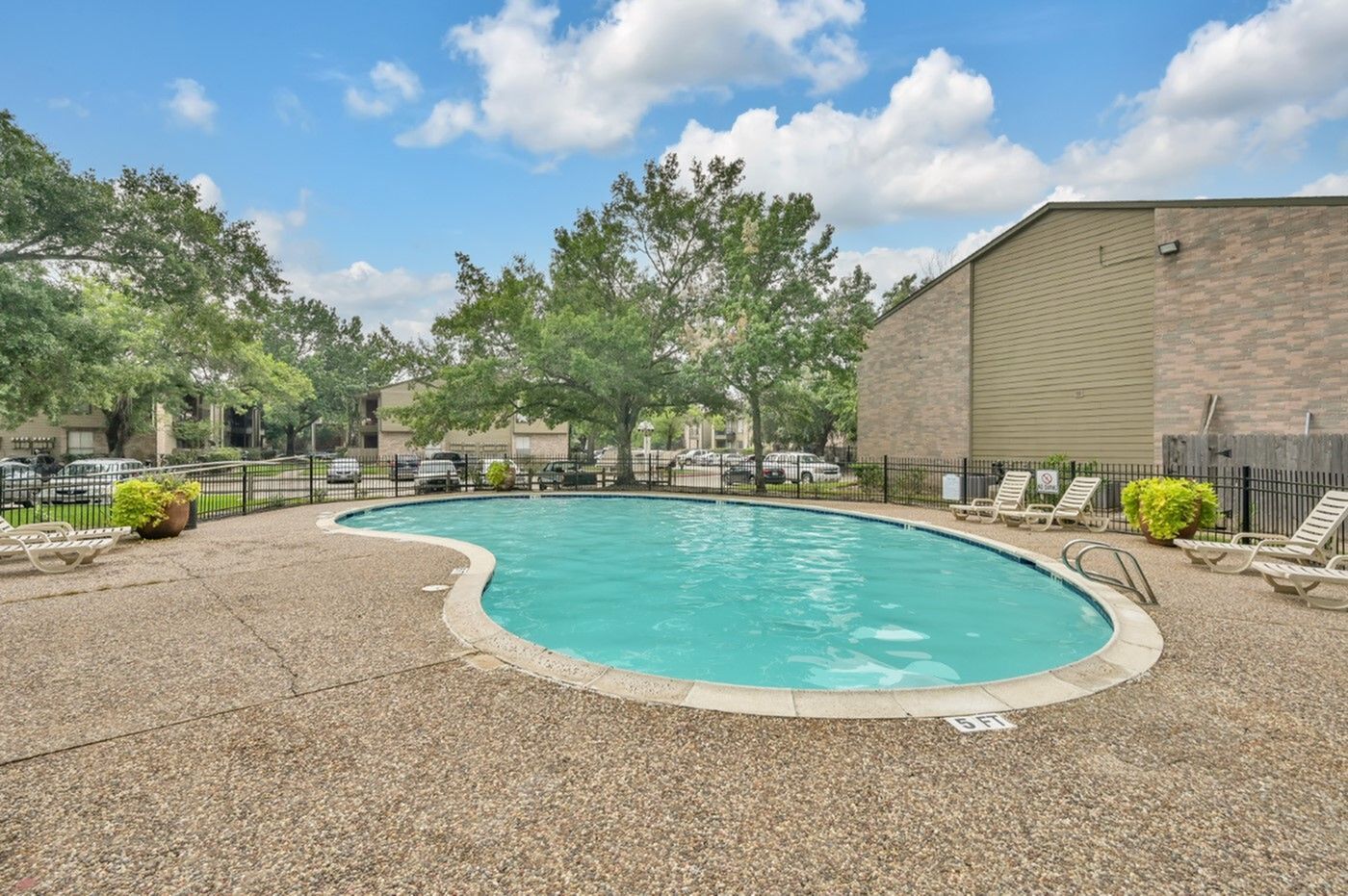 Charming apartment complex featuring a sunlit outdoor pool with surrounding lounge chairs and lush greenery, perfect for relaxation.