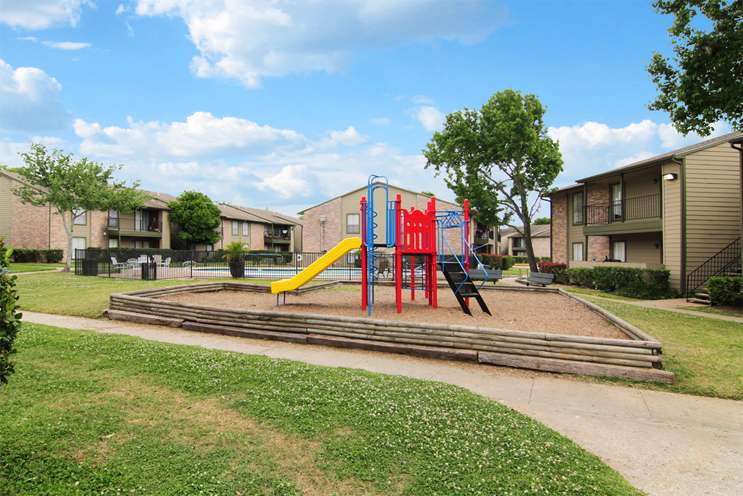 Charming apartment community with a colorful playground surrounded by lush greenery and modern buildings.