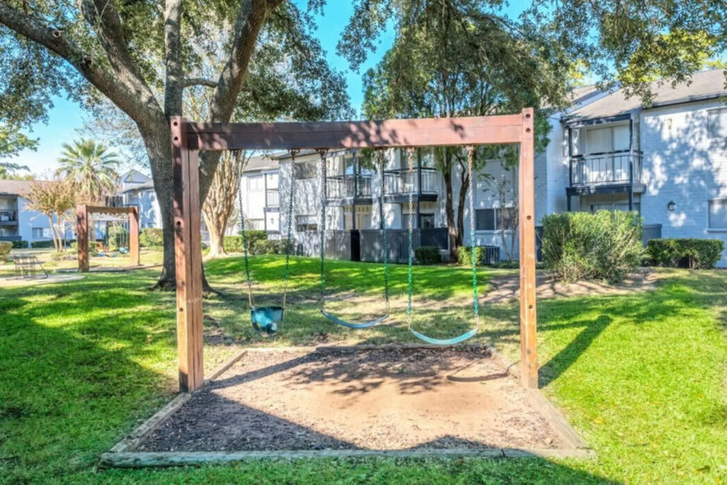 Charming apartment complex with lush green surroundings and inviting playground swings.