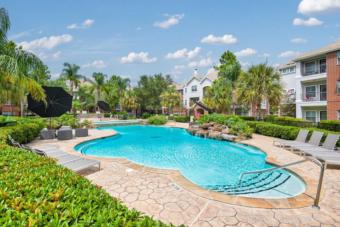 Luxurious apartment complex with sparkling pool surrounded by lush greenery and stylish lounge chairs for relaxation.