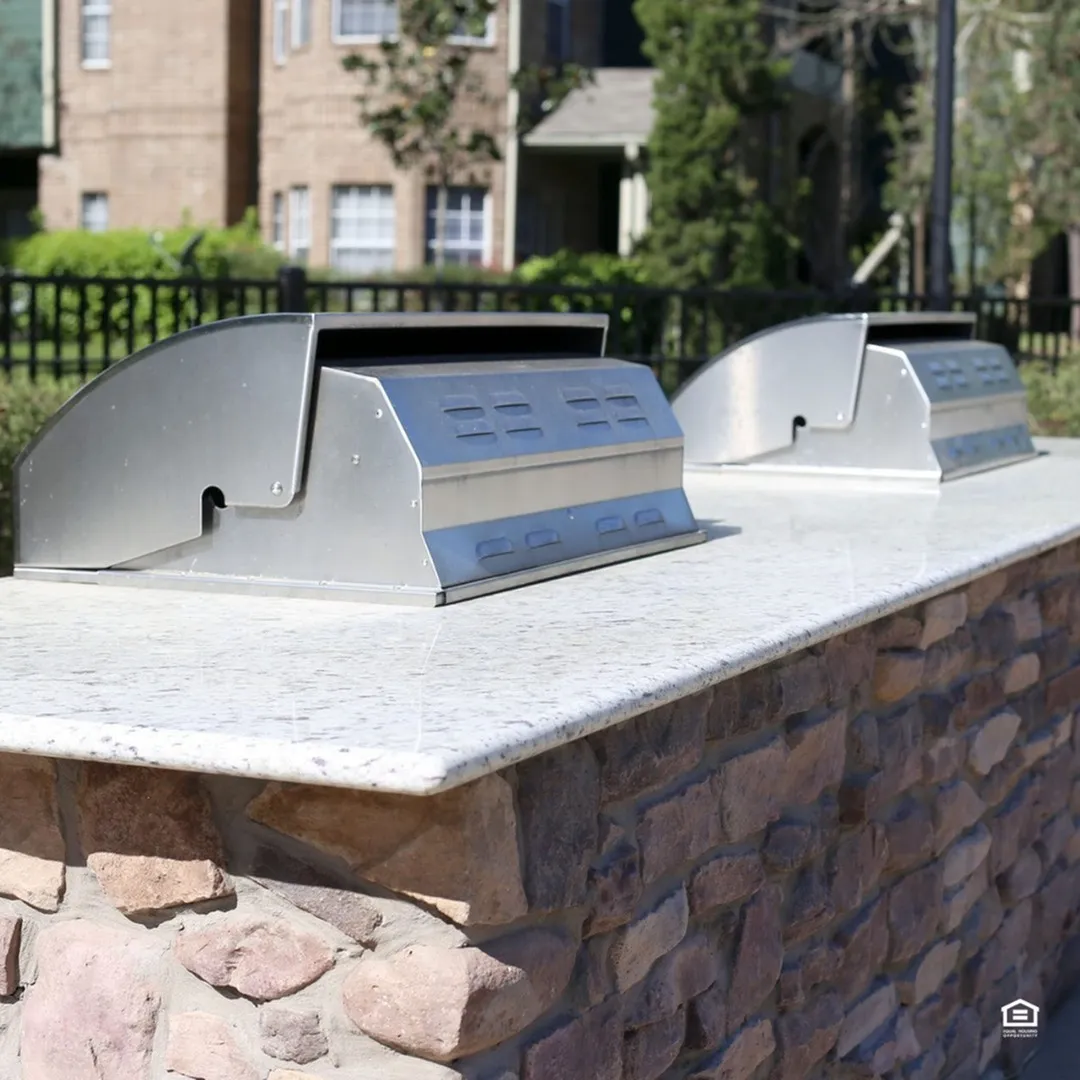 Chic outdoor BBQ grills on a stylish stone countertop, perfect for entertaining in a modern apartment community.