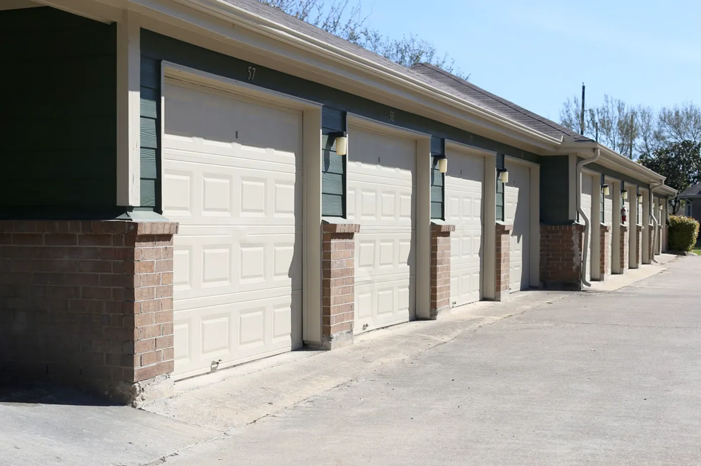 Modern apartment complex showcasing a row of spacious garages, complemented by brick pillars and elegant exterior lighting.