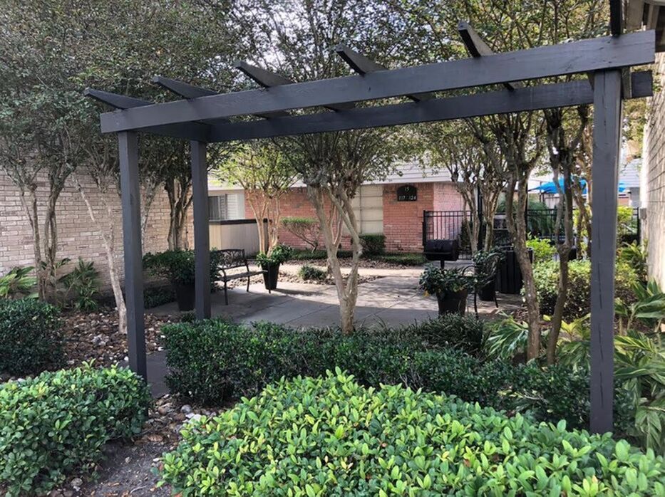 Charming garden space featuring a wooden pergola, lush green shrubs, and a cozy bench for relaxation.