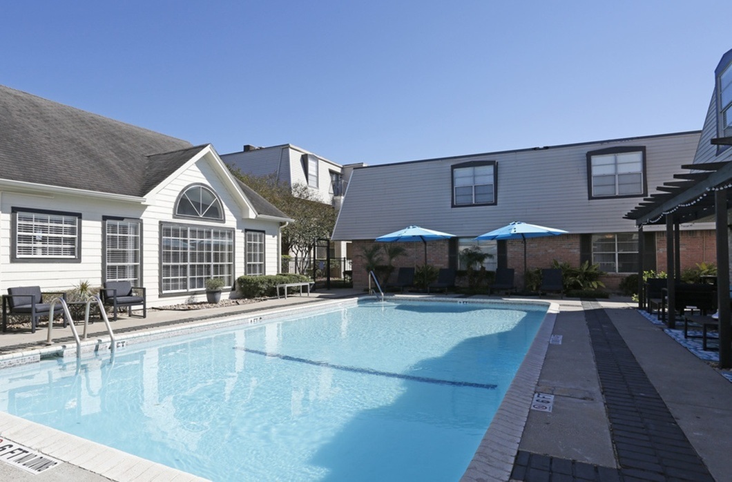 Inviting apartment complex pool area with stylish lounge chairs, vibrant blue parasols, and modern architecture, perfect for relaxation under clear skies.