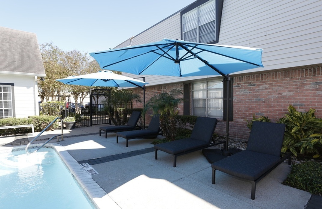Charming poolside area with stylish loungers and vibrant blue umbrellas, perfect for relaxation and enjoying sunny days.