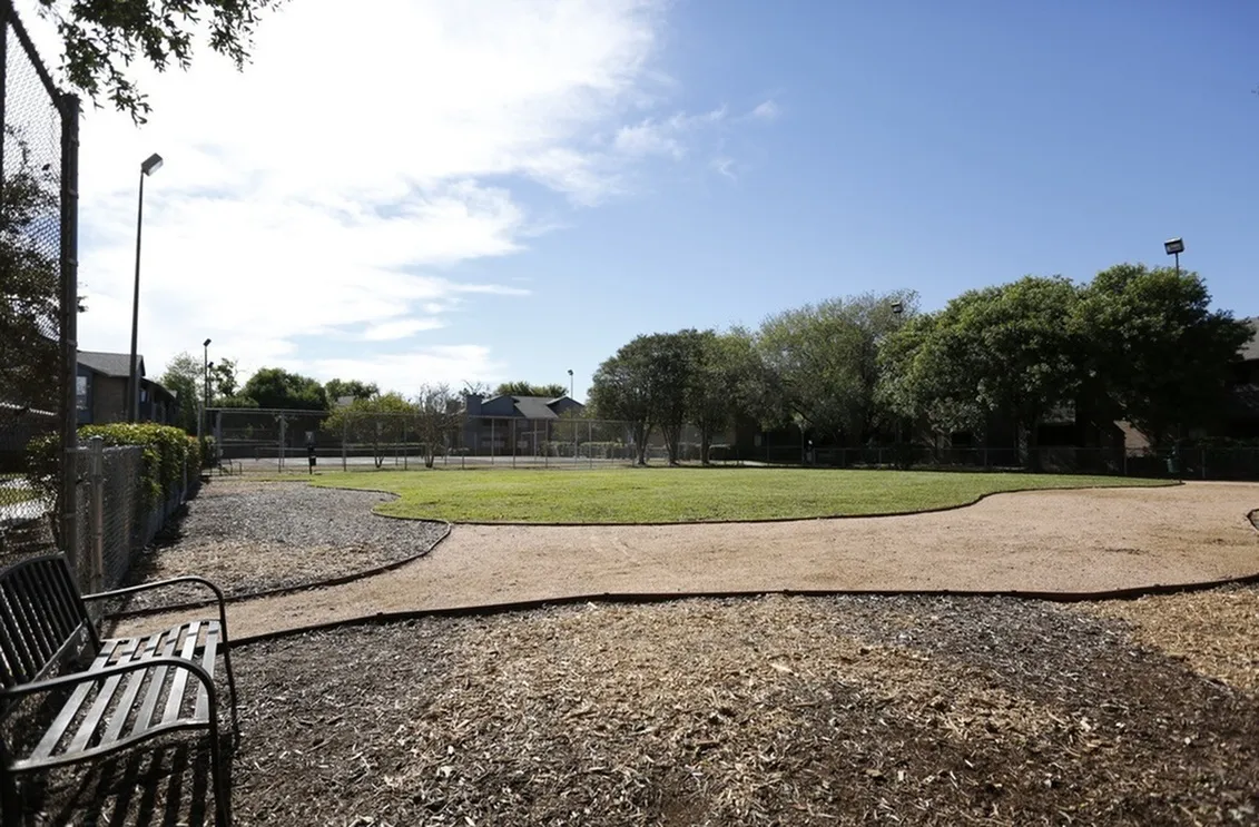 Spacious outdoor dog park surrounded by lush green trees and well-maintained walking paths, perfect for pet-friendly living.