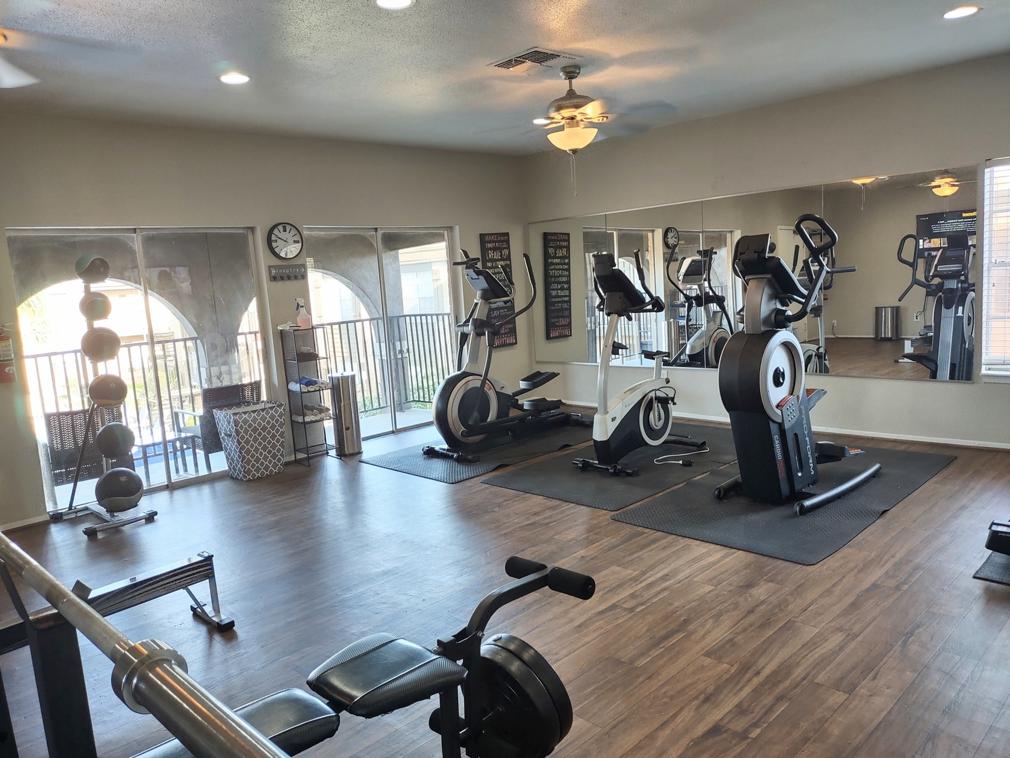 Bright and inviting gym with modern cardio equipment, wall mirrors, and hardwood flooring, creating a spacious atmosphere.