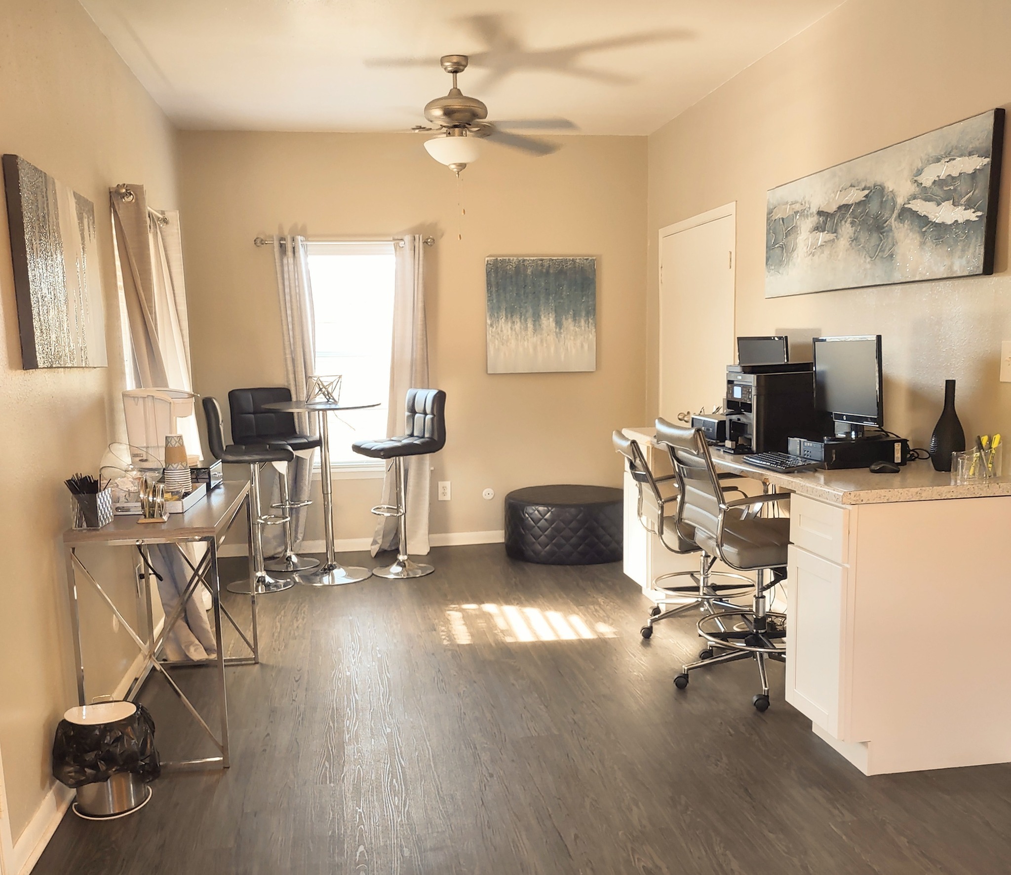 Bright and modern open-concept living space with elegant decor, featuring sleek bar stools, stylish artwork, and a functional workspace in a cozy apartment setting.