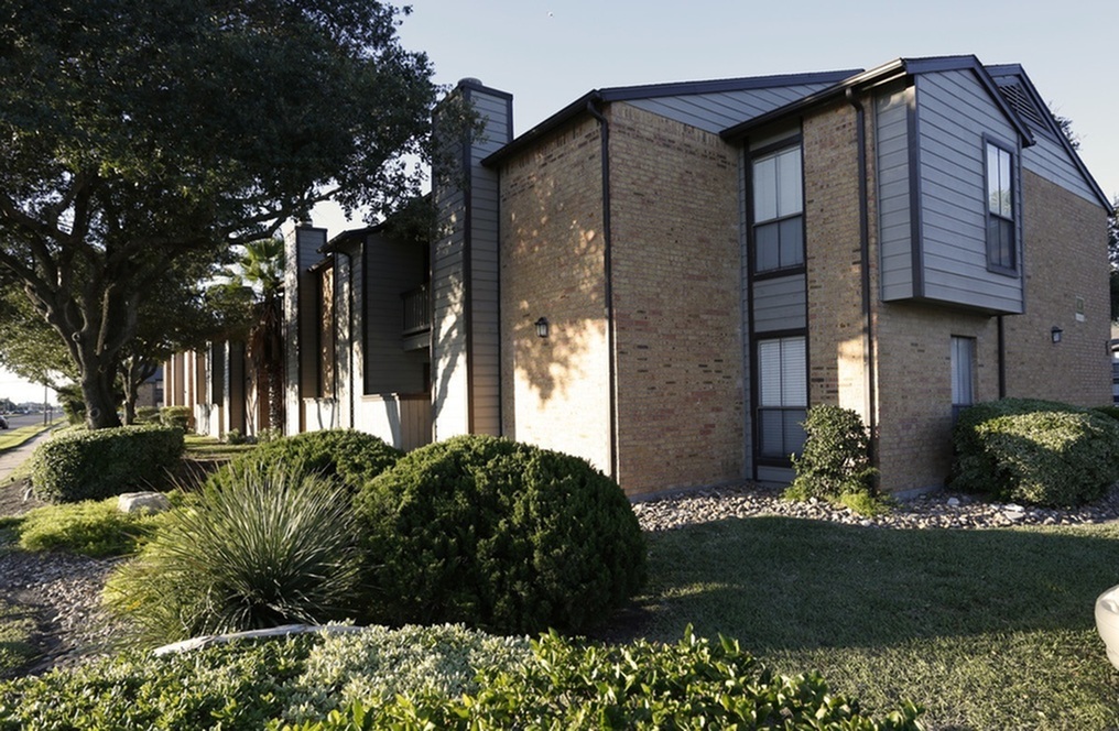 Charming brick apartment building with modern siding surrounded by lush greenery and mature trees.