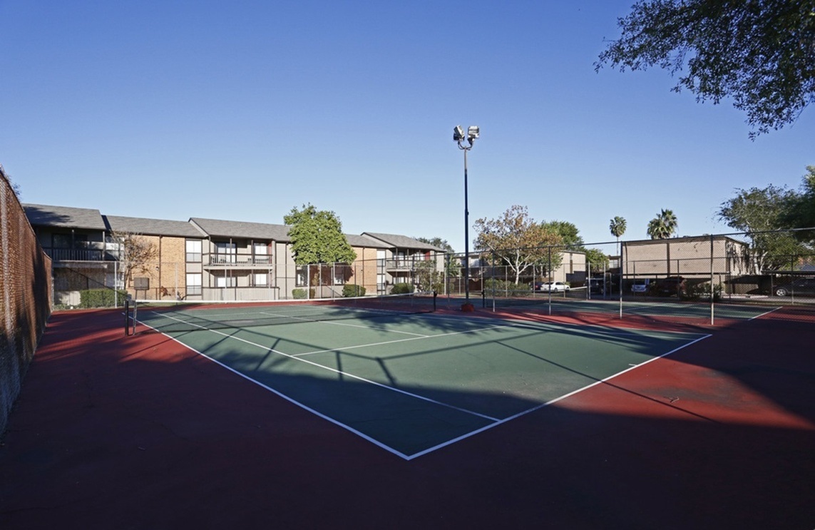 Spacious tennis court surrounded by lush greenery and modern apartment buildings, perfect for active living.