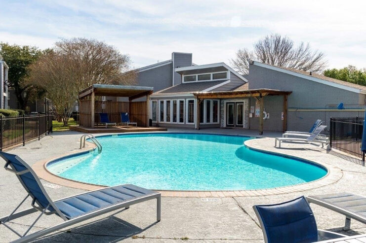 Inviting apartment community pool area with modern seating, sunlit deck, and lush surrounding greenery.