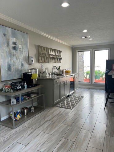 Chic modern kitchenette with elegant decor, featuring a refreshment station and bright natural lighting through large glass doors.